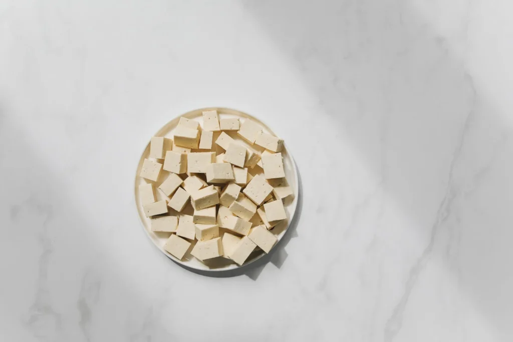 Block of extra firm tofu being pressed under paper towels and a cast-iron skillet next to spices and coconut milk can