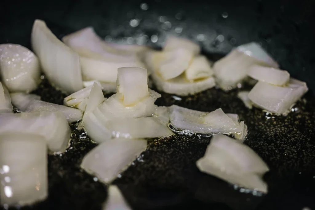 Sautéing diced onions, garlic, ginger, and bloomed red spices in a skillet