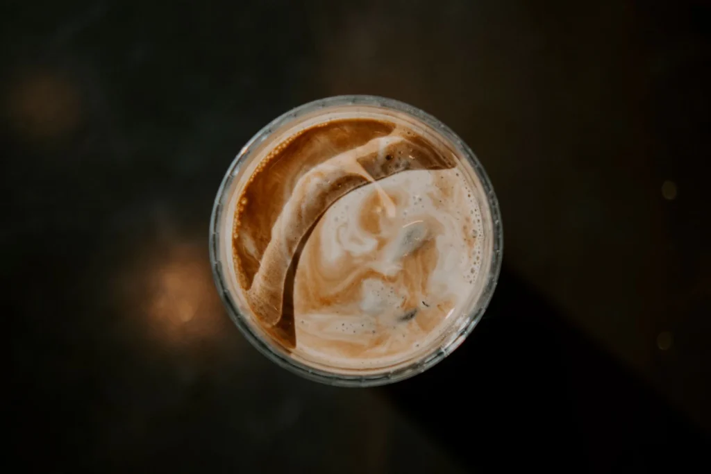 Pouring whole milk into a glass of iced chai concentrate, showing dramatic marble swirls