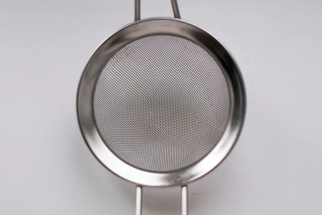 Straining deep golden chai concentrate through a fine mesh sieve into a glass Mason jar