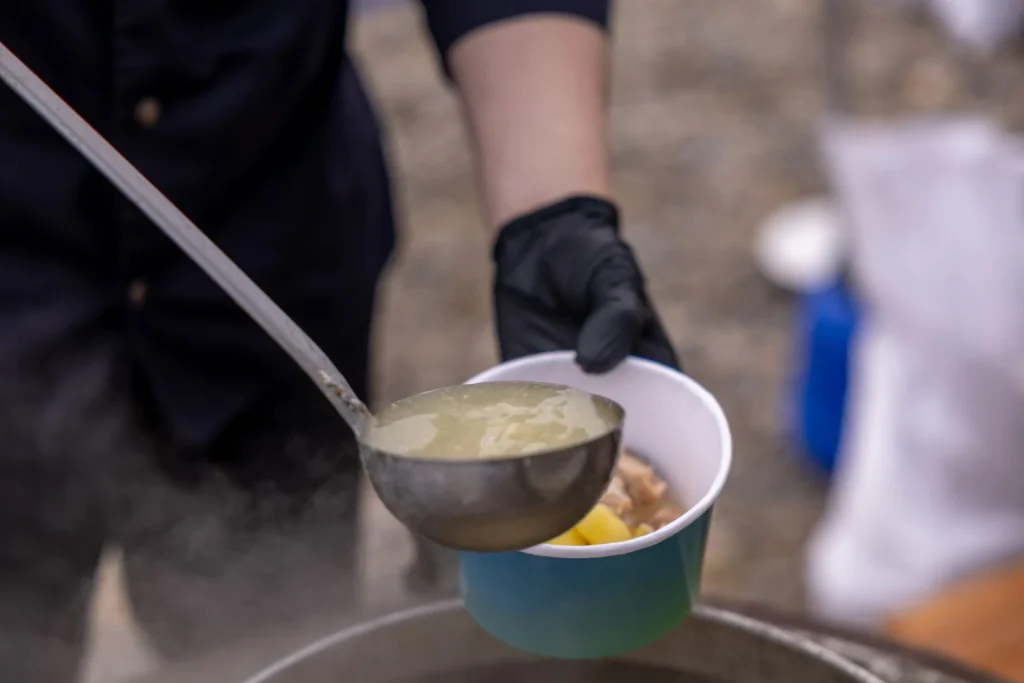 Macro ladle shot pulling up steaming curly egg noodles and tender shredded chicken coated in golden broth