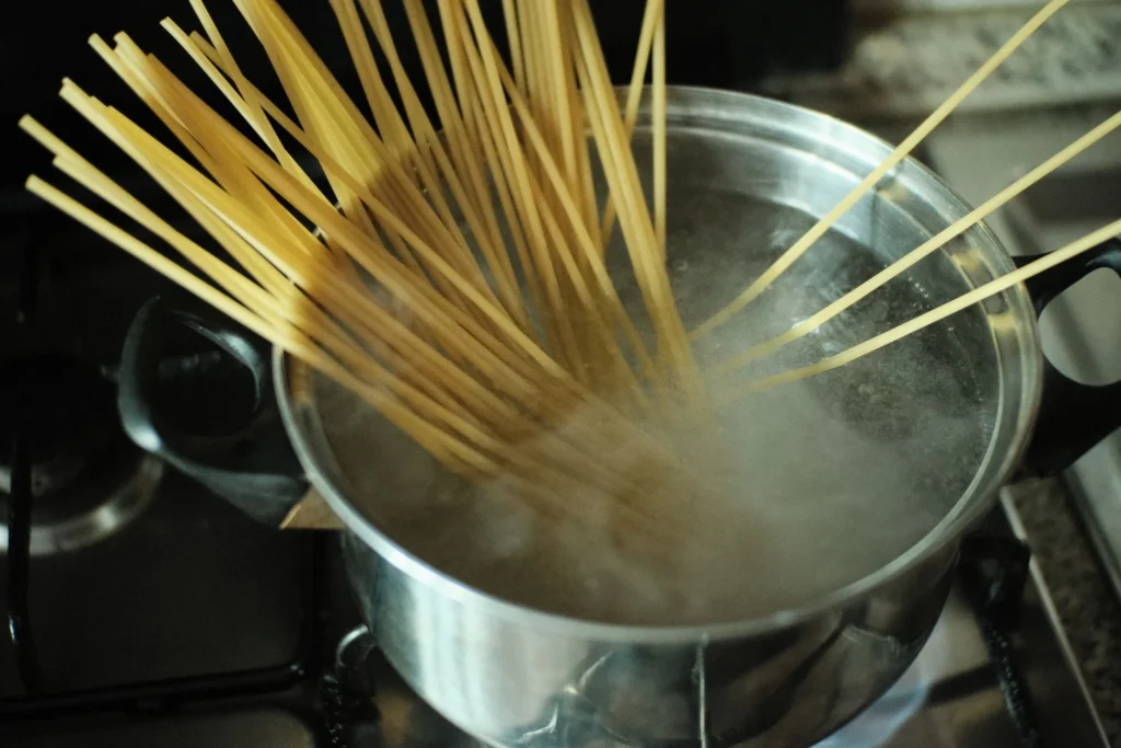 Adding curly wide egg noodles into the boiling turmeric-golden chicken broth